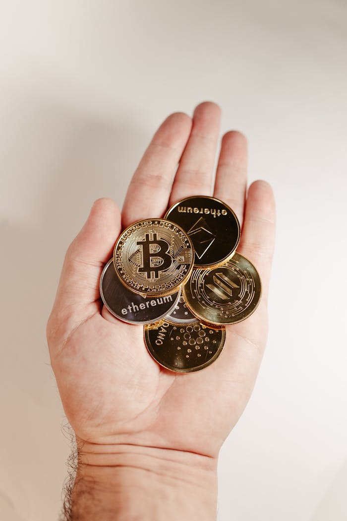 A hand holds various cryptocurrency coins including Bitcoin, Ethereum, and others.