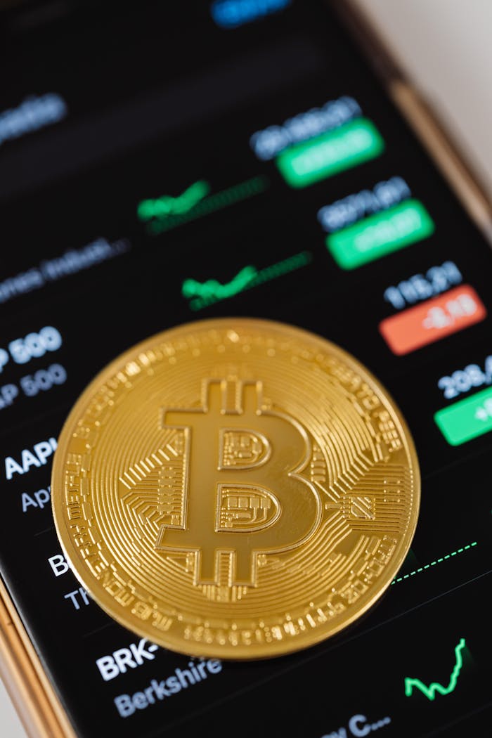 Close-up of a golden Bitcoin coin on a smartphone displaying stock trading data, symbolizing modern digital finance.